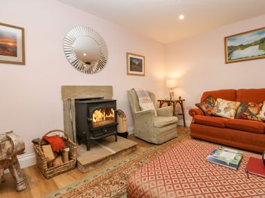 A living room with a wood stove a basket of firewood an armchair an orange sofa and a rug at Todridge Barn in Corbridge