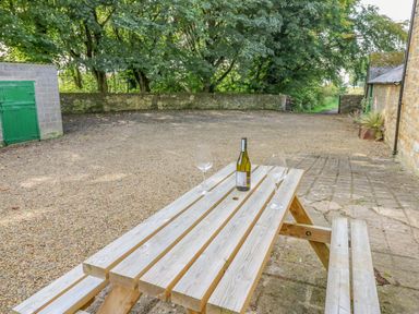 A picnic table with a bottle and two wine glasses in an outdoor stone courtyard at Todridge Barn in Corbridge