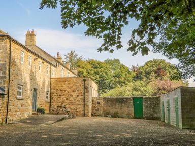 An outdoor area with stone buildings a wooden bench and green doors at Todridge Barn Corbridge