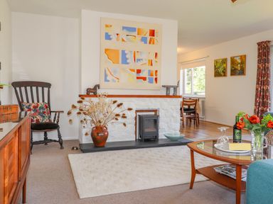 A living room with a white rug wooden rocking chair and a fireplace with artwork above at Goldcrest in Newport Pembrokeshire