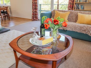 A living room with a coffee table holding flowers wine and glasses and a sofa with cushions at Goldcrest in Newport Pembrokeshire