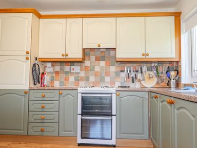 A kitchen with cream and green cabinets a white oven and tiled backsplash at Goldcrest in Newport Pembrokeshire