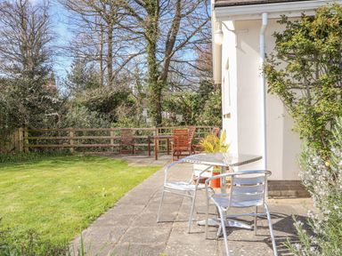 A garden with metal chairs and table on a paved patio and wooden chairs with table near a fence at Goldcrest in Newport Pembrokeshire
