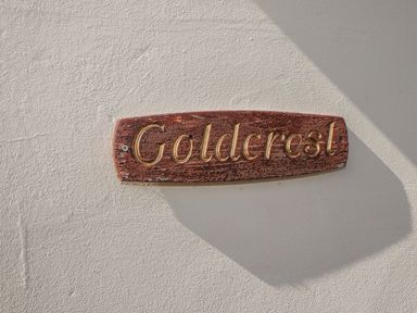 A wooden sign with the text Goldcrest mounted on a textured white wall at Goldcrest in Newport Pembrokeshire