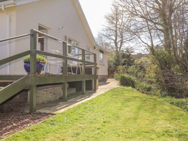 A patio area with metal chairs and a blue flowerpot attached to a house with a grassy lawn and trees at Goldcrest in Newport Pembrokeshire