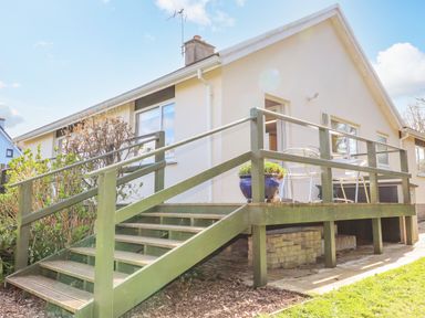 An exterior view of a single-story house with a green wooden deck and stairs with outdoor furniture and plants at Goldcrest in Newport Pembrokeshire