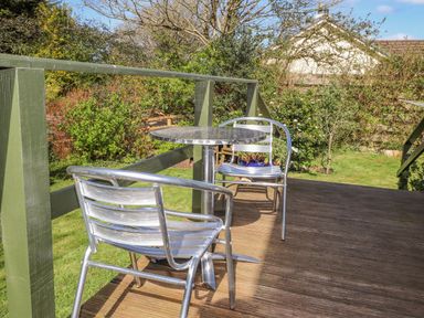 A wooden deck with two metal chairs and a round metal table overlooking a garden at Goldcrest in Newport Pembrokeshire