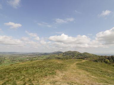 A grassy hill with a dirt path and distant hills under a partly cloudy sky at The Croft in Leigh Sinton