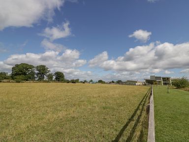 An open field with cows grazing near trees and a modern building in the distance at The Croft in Leigh Sinton