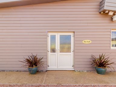 A double white door on a beige exterior wall with two potted plants on each side and a sign that reads The Croft at Leigh Sinton