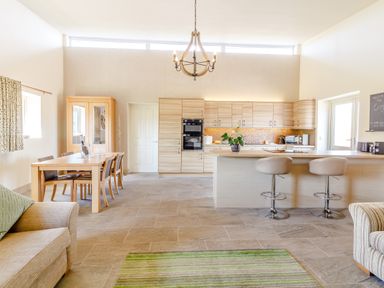 An open kitchen and dining area with a wooden dining table and chairs a kitchen island with two bar stools and a beige couch at The Croft in Leigh Sinton