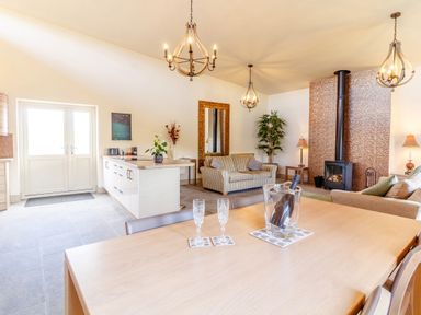 A dining and living area with a wooden table and chairs a striped sofa a wood stove and pendant lights at The Croft in Leigh Sinton