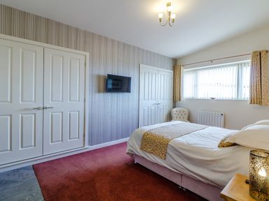 A bedroom with a double bed a wall-mounted television two double wardrobes and a window with curtains at The Croft in Leigh Sinton