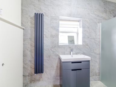 A bathroom with a sink cabinet a vertical radiator a window and frosted glass shower at The Croft in Leigh Sinton
