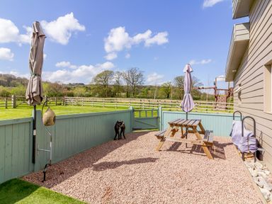 A fenced outdoor patio with a wooden picnic table and two closed umbrellas at The Croft in Leigh Sinton