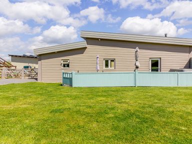 A beige building with two small windows a door and a blue fence on a green lawn at The Croft in Leigh Sinton