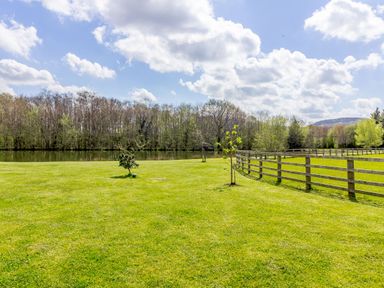 A grassy field with young trees and a wooden fence near a pond with trees in the background at The Croft in Leigh Sinton