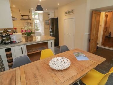A kitchen and dining area with a wooden table, chairs, flower arrangement, microwave, wine rack, and refrigerator at Fairfield Cottage in Boscastle