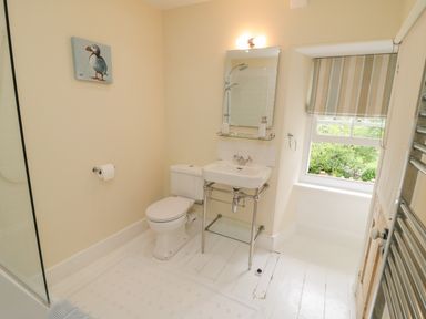 A bathroom with a toilet sink mirror striped window blind and puffin painting at Fairfield Cottage in Boscastle