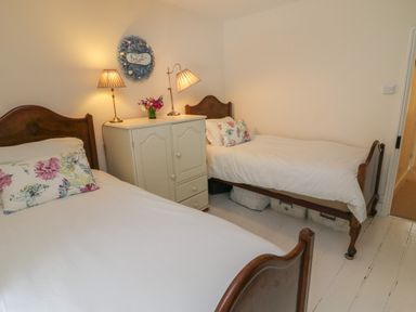A bedroom with two single beds floral pillows white cabinet and two lamps at Fairfield Cottage in Boscastle