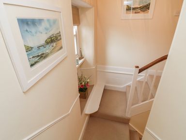 A staircase with beige carpet a wooden handrail framed paintings and a windowsill with flowers at Fairfield Cottage in Boscastle