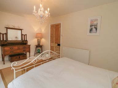 A bedroom with a white metal bed frame wooden dresser with mirror table lamp and chandelier at Fairfield Cottage in Boscastle