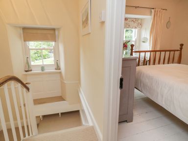 A stairway with a window and decorative items leading to a bedroom with a wooden bed and a bedside cabinet at Fairfield Cottage in Boscastle