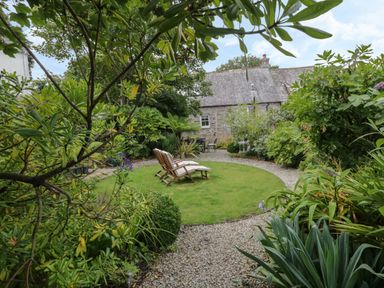 A garden with a circular lawn and two wooden lounge chairs surrounded by plants and a gravel path at Fairfield Cottage in Boscastle