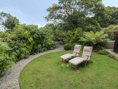 A garden with two lounge chairs on grass and a gravel path surrounded by plants at Fairfield Cottage in Boscastle