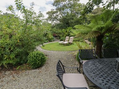 An outdoor garden area with gravel paths lawn chairs and a metal table with chairs at Fairfield Cottage in Boscastle