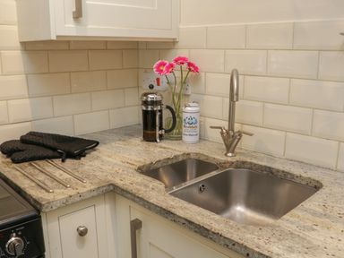 A kitchen countertop with a double stainless steel sink a modern faucet a coffee press flowers in a glass vase and oven gloves at Fairfield Cottage in Boscastle