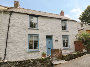 A white stone cottage with blue window frames and door a small wooden gate and potted plants at Fairfield Cottage Boscastle