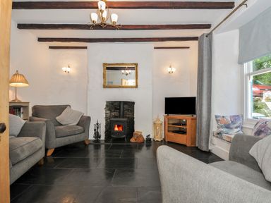A living room with gray armchairs a wood stove and television at Fairfield Cottage in Boscastle