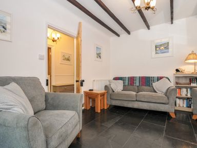 A living room with two gray sofas a wooden side table a bookshelf and exposed ceiling beams at Fairfield Cottage in Boscastle