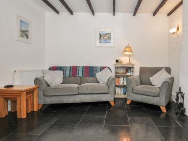 A living room with a sofa and armchair next to a small bookshelf with a lamp at Fairfield Cottage in Boscastle
