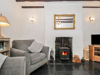 A living room with a fireplace wood stove gray armchairs and a television at Fairfield Cottage in Boscastle