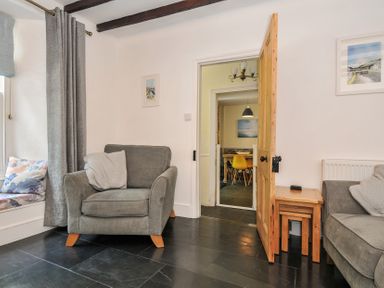 A living room with a grey armchair a small wooden side table with nested tables and a doorway showing a dining area at Fairfield Cottage in Boscastle