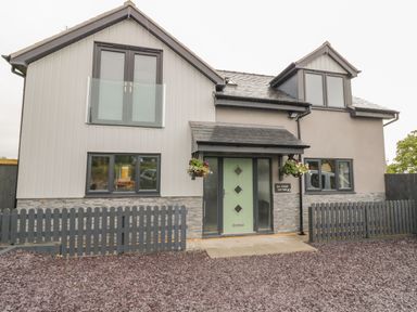 Exterior view of a two-story house with a green front door and black picket fence at Big Azzles in Tyn-y-Gongl near Benllech