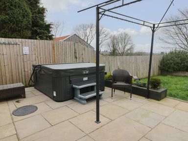 An outdoor patio area with a hot tub brown wicker chair and green grass at Big Azzles in Tyn-y-Gongl near Benllech