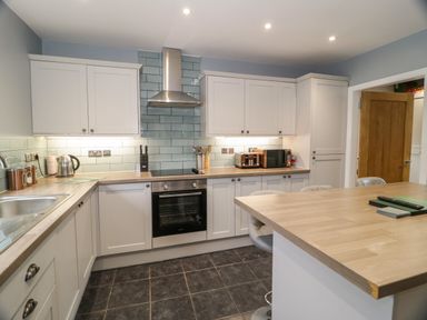 A kitchen with white cabinets wooden countertops an oven stovetop and an island at Big Azzles in Tyn-y-Gongl near Benllech