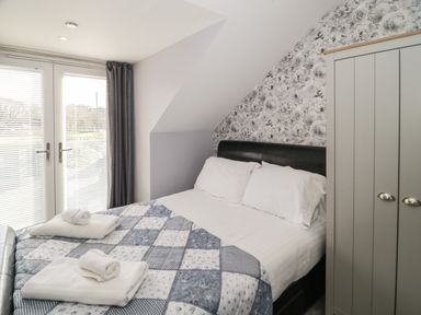 A bedroom with a bed covered with a patchwork quilt and towels near doors with blinds and a wardrobe at Big Azzles in Tyn-y-Gongl near Benllech