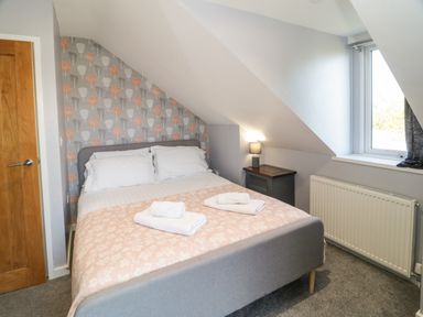 A bedroom with a double bed, folded towels, a bedside table with a lamp, a window, and a radiator at Big Azzles in Tyn-y-Gongl near Benllech