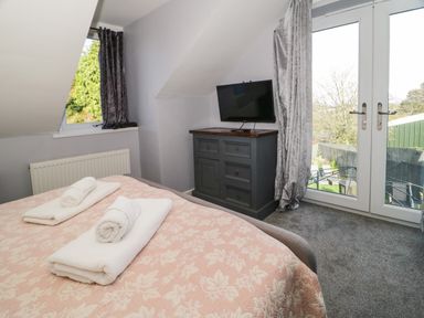 A bedroom with a bed covered with a patterned blanket and towels on top a cabinet with a television and glass doors opening to a garden at Big Azzles in Tyn-y-Gongl near Benllech