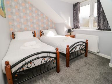 A bedroom with two single beds a bedside table and a window with curtains at Big Azzles in Tyn-y-Gongl near Benllech