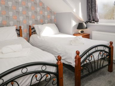 A bedroom with two single beds with white linens and a bedside table with a lamp at Big Azzles in Tyn-y-Gongl near Benllech
