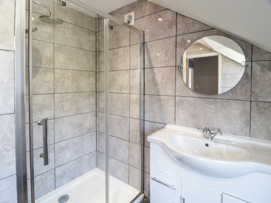 A bathroom with a glass shower enclosure round mirror and a white sink unit at Big Azzles in Tyn-y-Gongl near Benllech