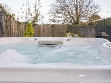 An outdoor hot tub with bubbling water in a fenced backyard with trees and patio chairs at Big Azzles in Tyn-y-Gongl near Benllech