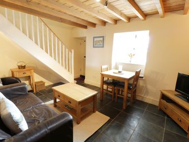 A living room with a leather sofa wooden coffee table dining table with two chairs and a television at Menai Cottage in Brynsiencyn