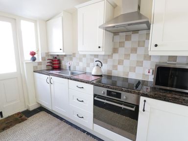 A kitchen with white cabinets a stove oven microwave red pots and a kettle at Menai Cottage in Brynsiencyn