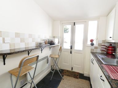 A kitchen with two bar stools along a wall-mounted counter and white double doors at Menai Cottage in Brynsiencyn